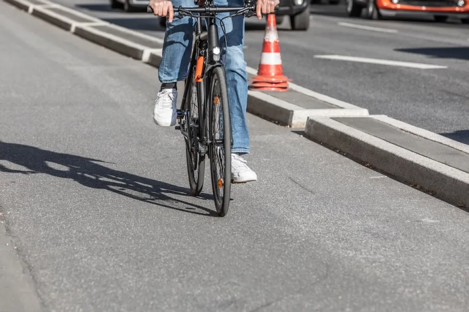 Close-up of person on road bike riding on protected bike lane separated by concrete curb from street.